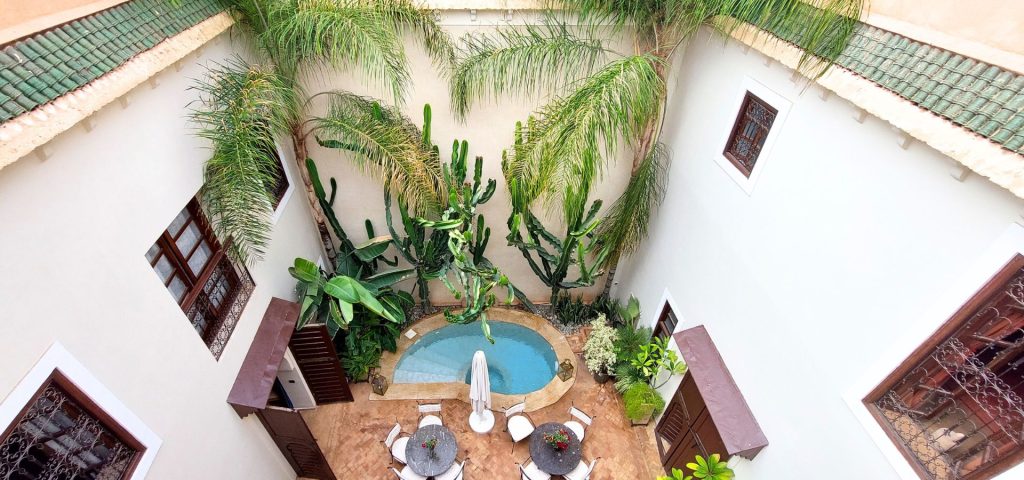 perchè alloggiare in un riad a Marrkech?
Un riad (arabo: riyāḍ) è una casa tradizionale marocchina, sviluppata su più piani attorno a un cortile interno centrale con giardino o fontana, situata solitamente all’interno della Medina, ossia il cuore pulsante del centro storico, circondata spesso da alte mura. Quello non solo turistico – di fatto tutte le attrazioni più importanti sono lì – ma anche commerciale, aspetto  decisamente tipico non solo della medina di marrakech, ma di tutte le medine marocchine.
Prima di raccontarti la storia del Riad Les Ammonites ci teniamo infatti a dirti che un Riad, nel tuo viaggio a Marrakech, può fare a differenza sotto tanti punti di vista. te li spieghiamo in questo articolo.
